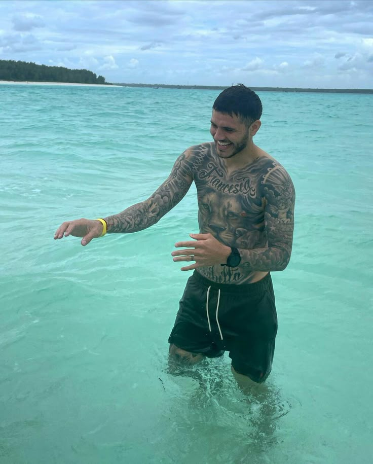 a man standing in the ocean holding his arm out to someone with tattoos on it