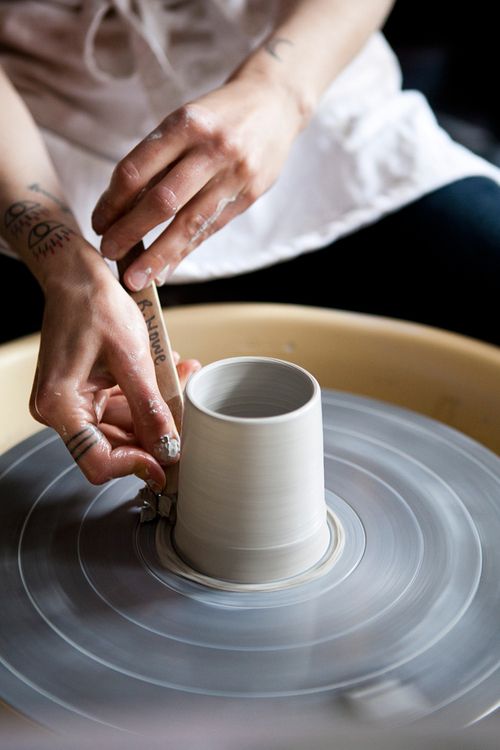 a woman making a vase out of clay on a potter's wheel with her hands