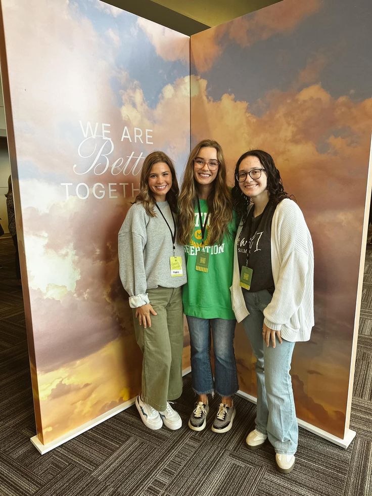 three women standing in front of a wall with the words we are better together on it