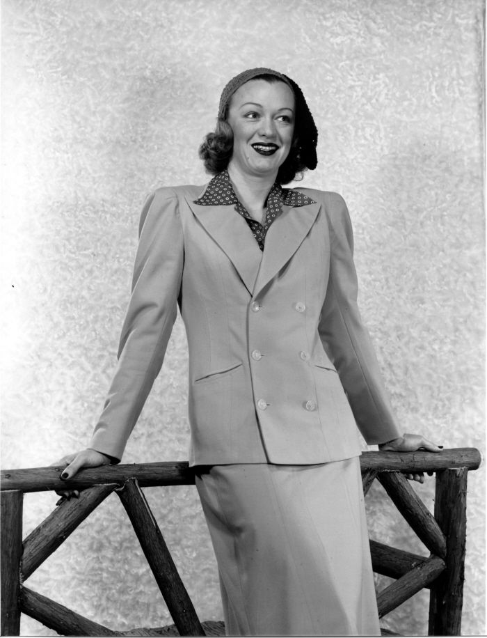 an old photo of a woman wearing a suit and smiling at the camera with her hands in her pockets