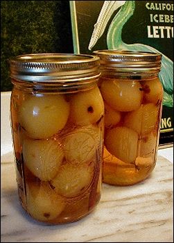 two jars filled with pickles sitting on top of a table next to a book