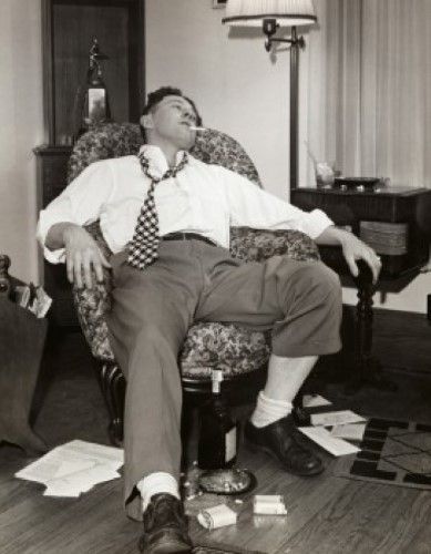 black and white photograph of a man sitting in a chair with his feet on the floor