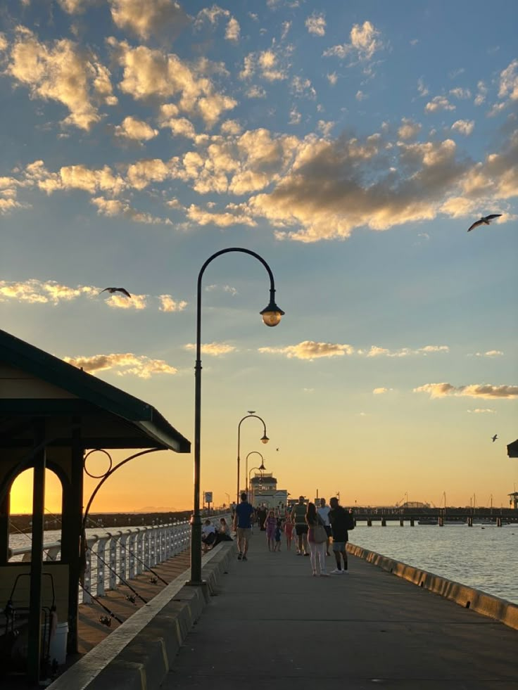 people are walking along the pier at sunset