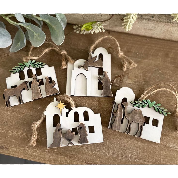 four small white houses with bells hanging from the front and side, on top of a wooden table