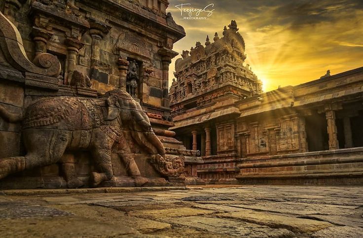 the sun is setting behind an elephant statue in front of some stone buildings and pillars