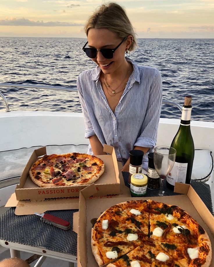 a woman sitting at a table with two pizzas in front of her on the boat