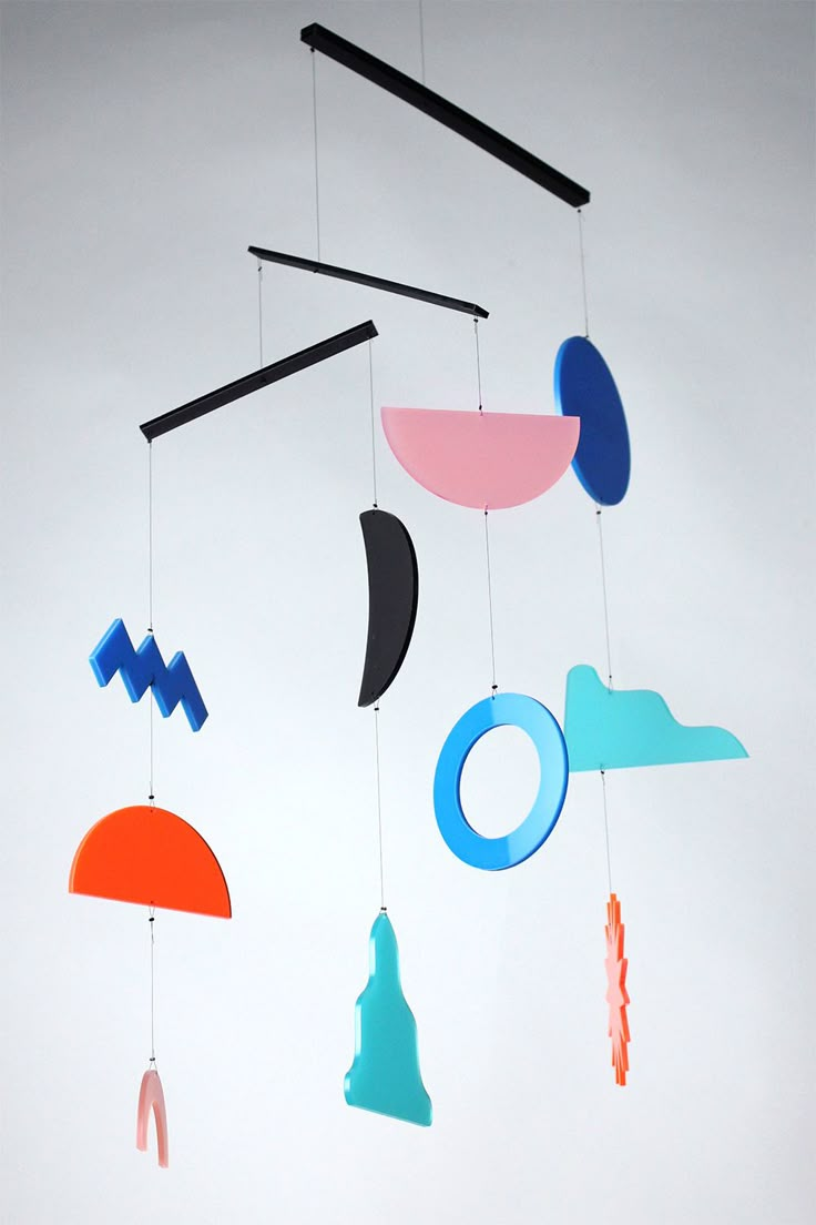 a mobile with different shapes and colors hanging from it's sides on a white wall