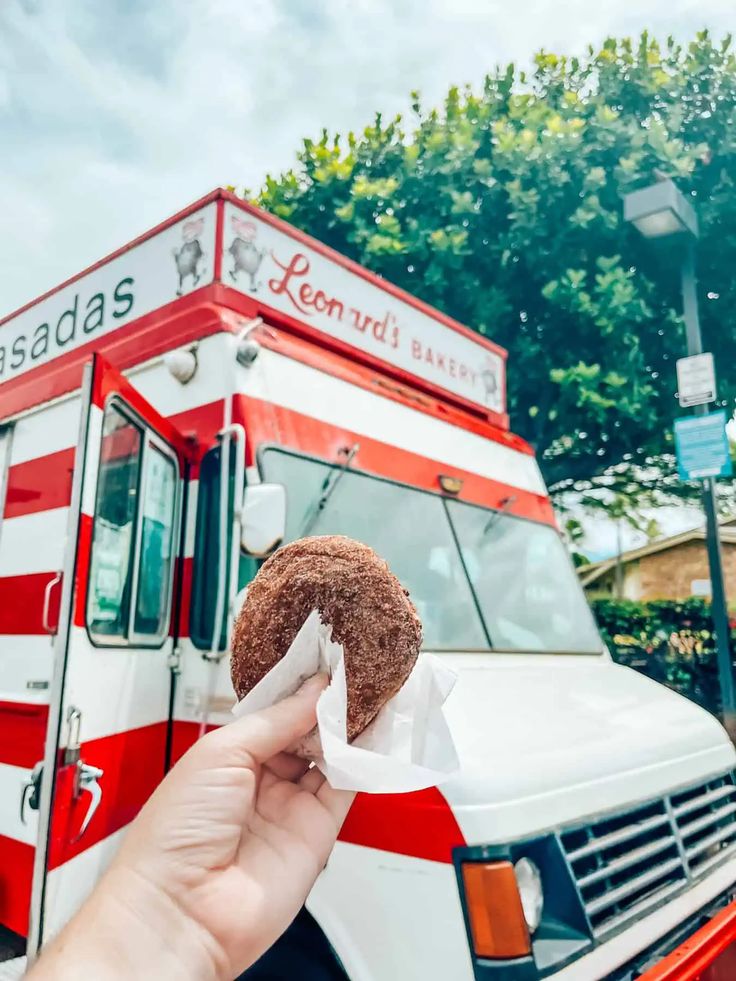 a person holding up a donut in front of a food truck