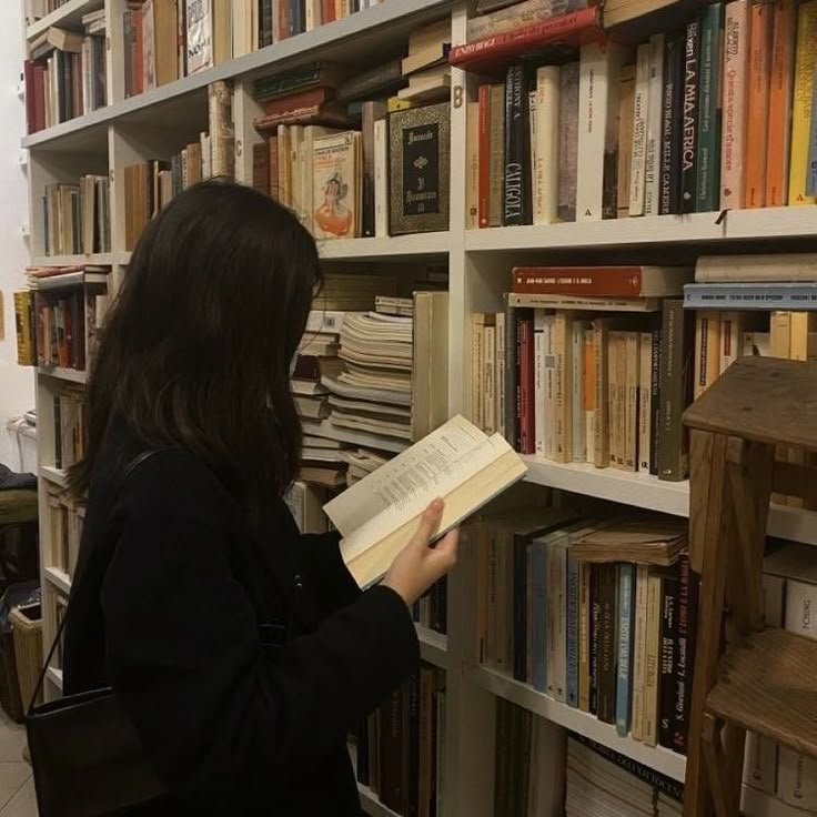 a woman standing in front of a bookshelf filled with lots of books and holding an open book