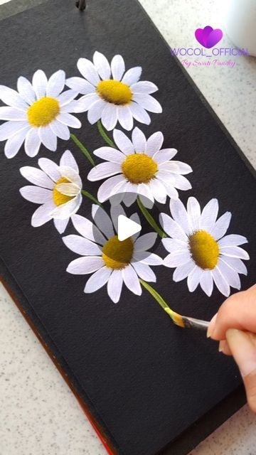 someone is cutting out some flowers on a piece of black paper with white and yellow centers