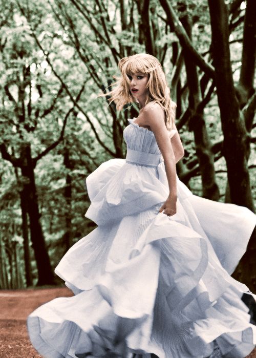 a woman in a blue and white dress is walking through the woods with trees behind her