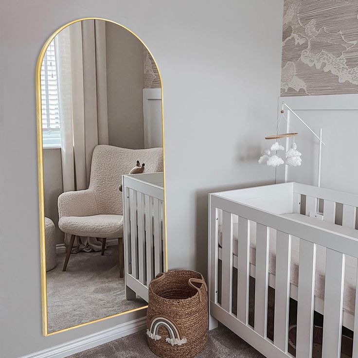 a baby's room with a crib, chair and large mirror in it