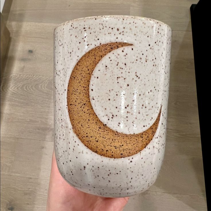 a hand holding a ceramic mug with a crescent on it