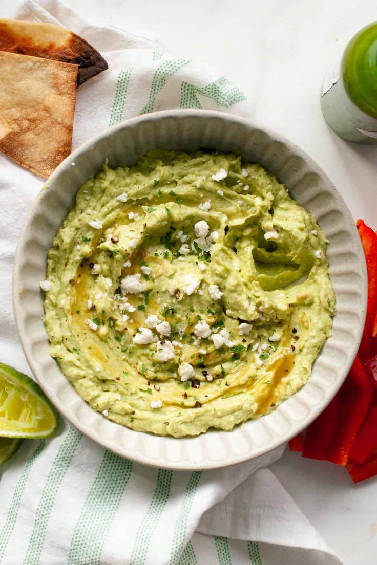 a white bowl filled with guacamole surrounded by tortilla chips