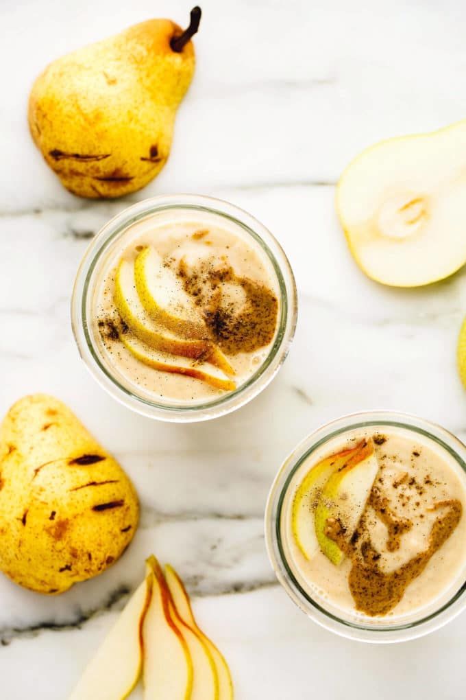 two glasses filled with ice cream next to sliced apples and cinnamon on a marble surface