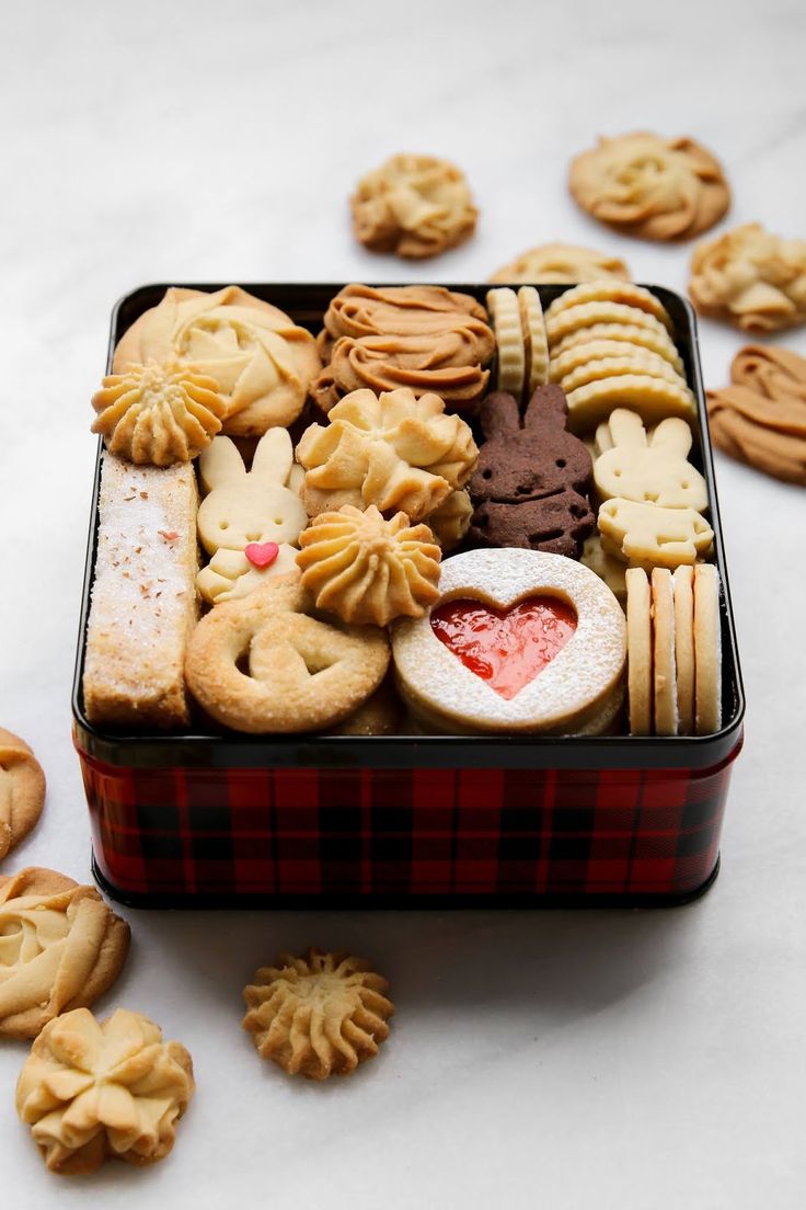 a tin filled with assorted cookies and pastries next to other small ones on a table