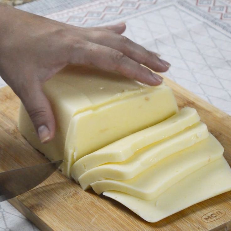 someone is cutting cheese on a wooden board