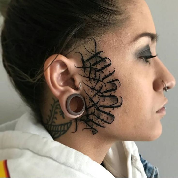 a woman with black ink on her face and behind her ear is an intricate design