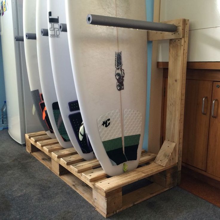 three surfboards are sitting on wooden pallets in a room with wood flooring