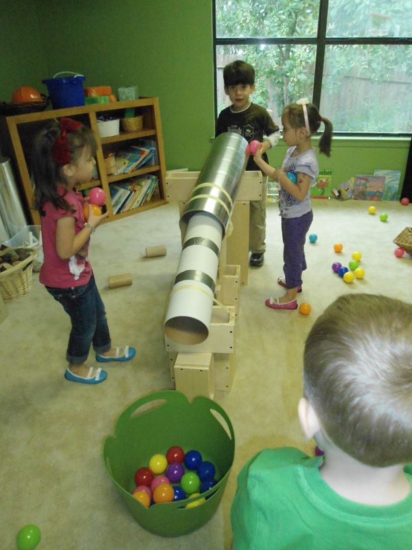 children playing with toys in a playroom on the floor near a large cannon toy