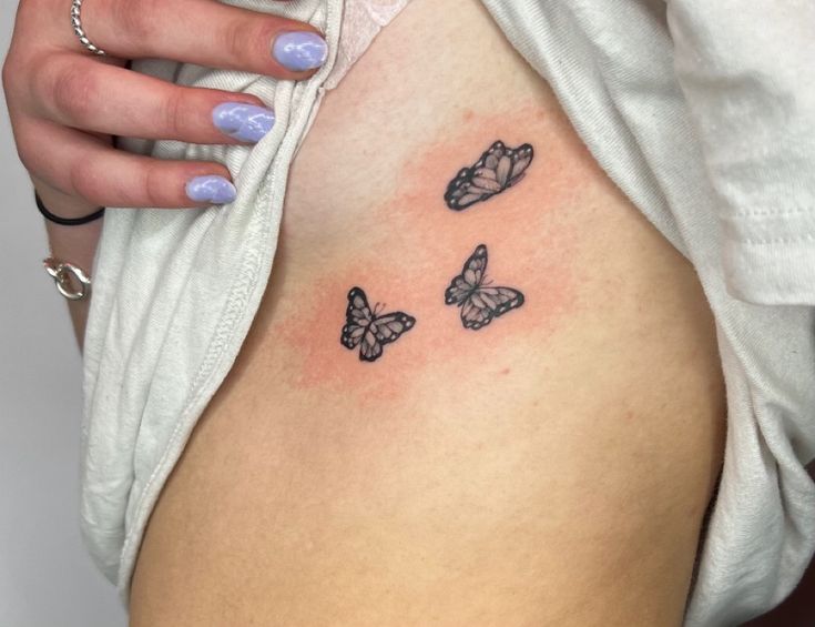 a woman's stomach with three butterflies on her side, and one is black