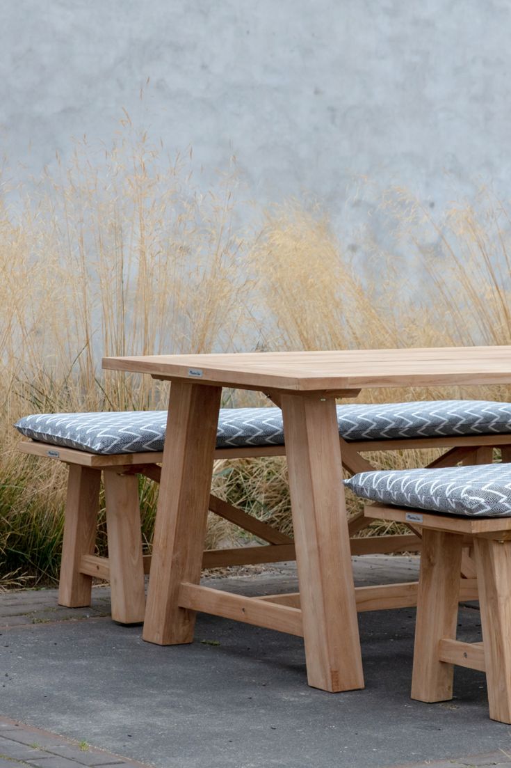 a wooden table with two benches next to it and tall grass in the back ground