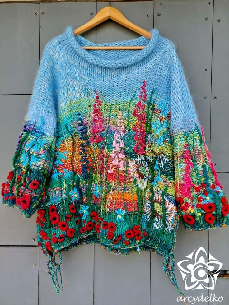 a blue sweater with flowers on it hanging from a wooden hanger in front of a wall