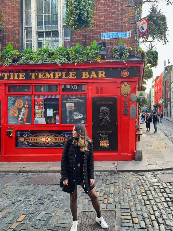 a woman standing in front of the temple bar on a cobblestone street with people walking by