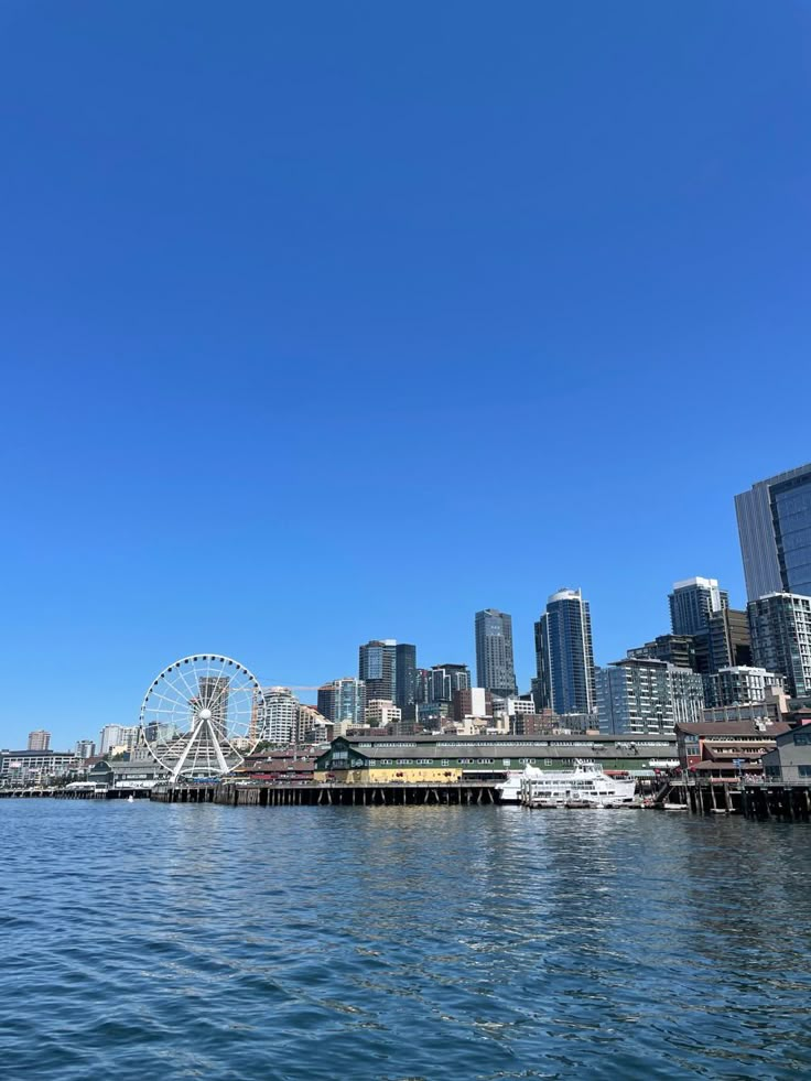 the city skyline as seen from across the water with ferris wheel in foreground and blue sky