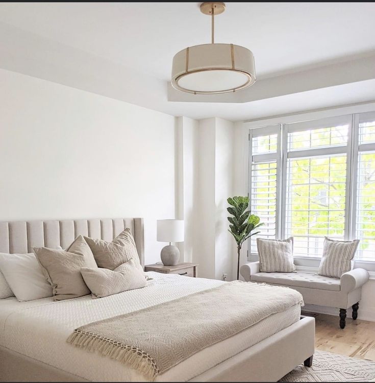 a large white bed sitting in a bedroom next to a chair and window with shutters