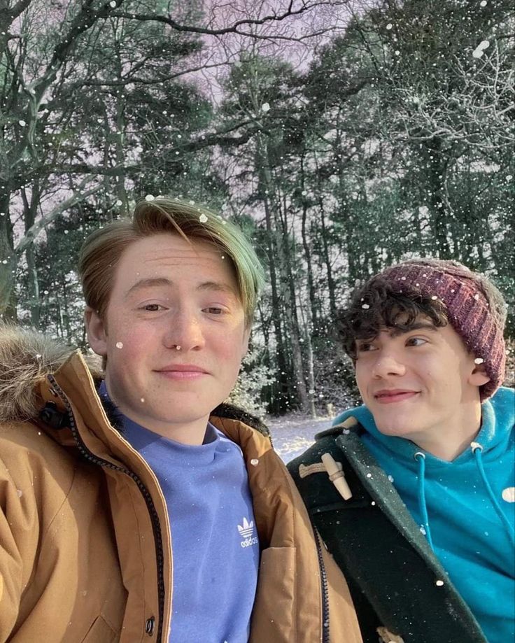 two young men standing next to each other in front of snow covered trees and bushes