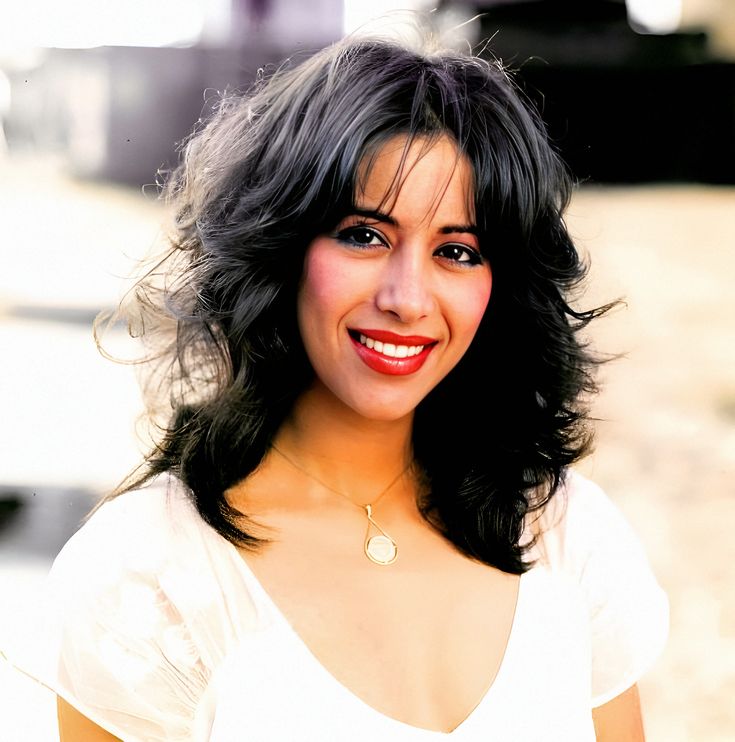 a close up of a person wearing a white shirt and smiling at the camera with her hand on her hip