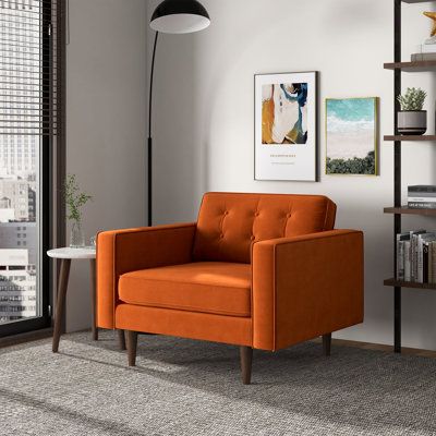 an orange chair sitting in front of a window next to a book shelf filled with books