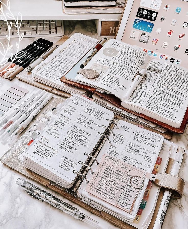 two open notebooks sitting next to each other on top of a table with pens and pencils