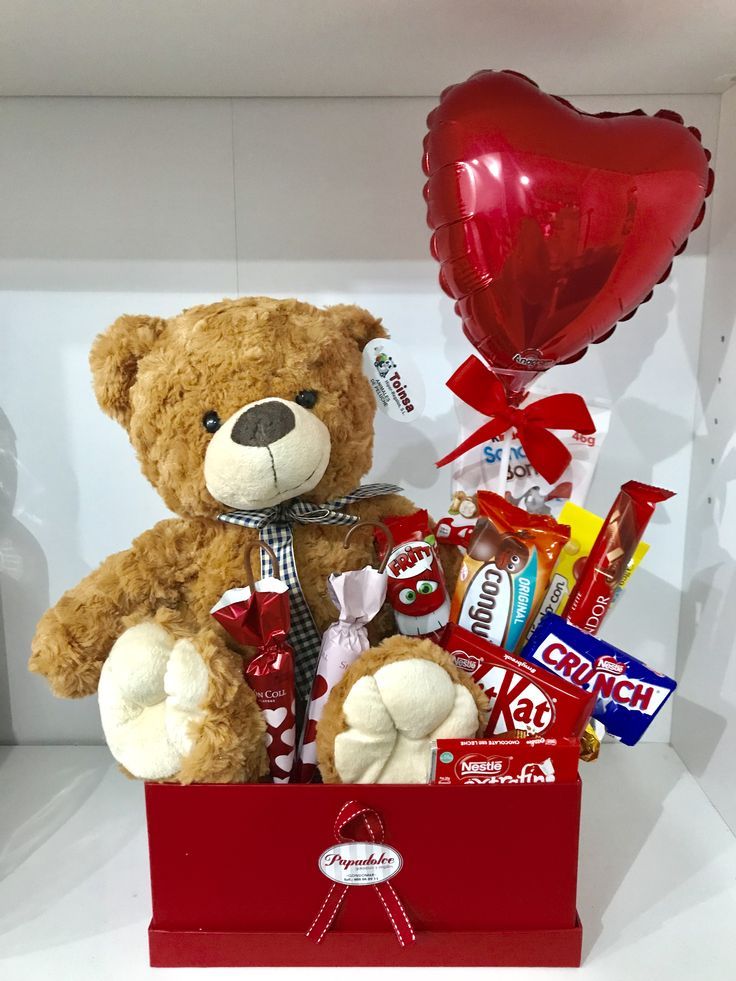 a teddy bear sitting in a red box filled with candy, balloons and heart shaped balloons