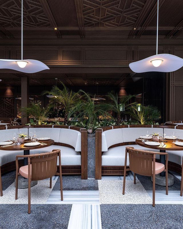 a restaurant with round tables and wooden chairs in front of plants on the wall behind them