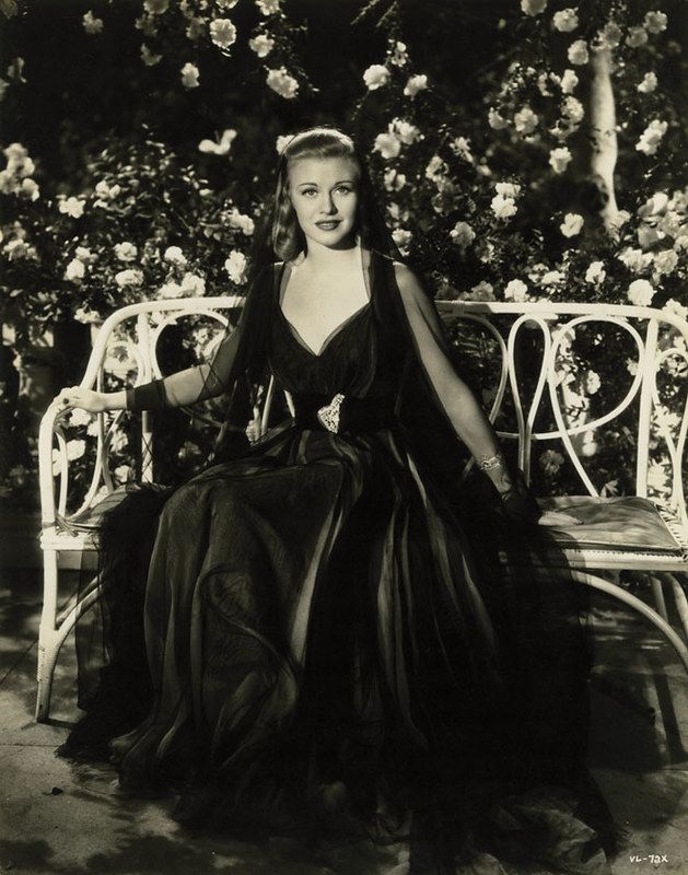 an old black and white photo of a woman in a dress sitting on a bench