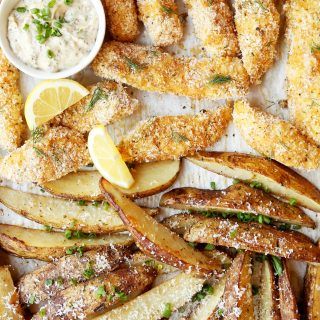 fried fish and french fries on a tray with dipping sauce, lemon wedges and parmesan cheese