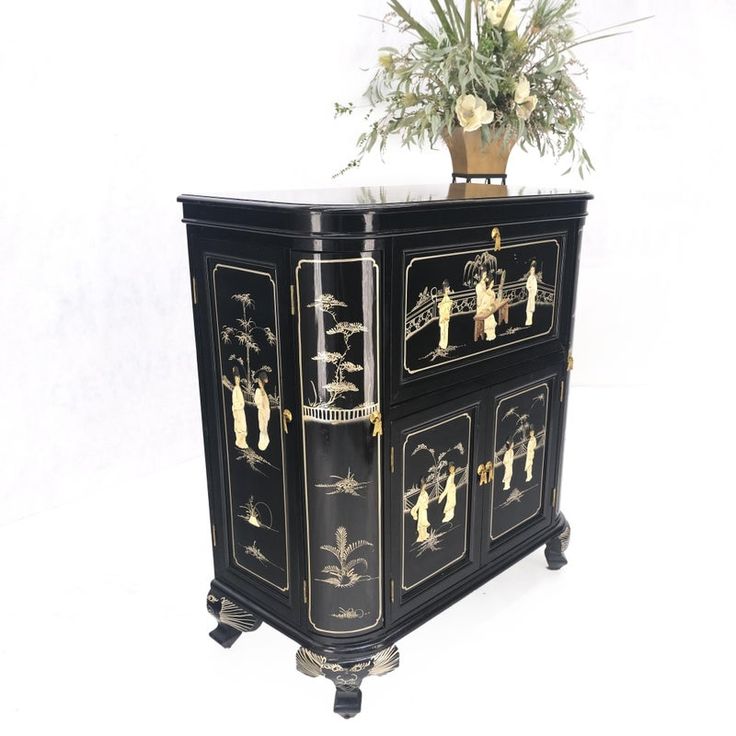 a black and gold painted cabinet with flowers on top