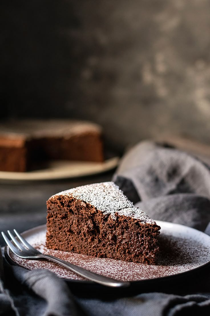 a slice of chocolate cake with powdered sugar on top, sitting on a plate