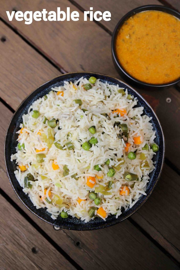 vegetable rice and carrots in a black bowl on a wooden table next to two bowls of soup