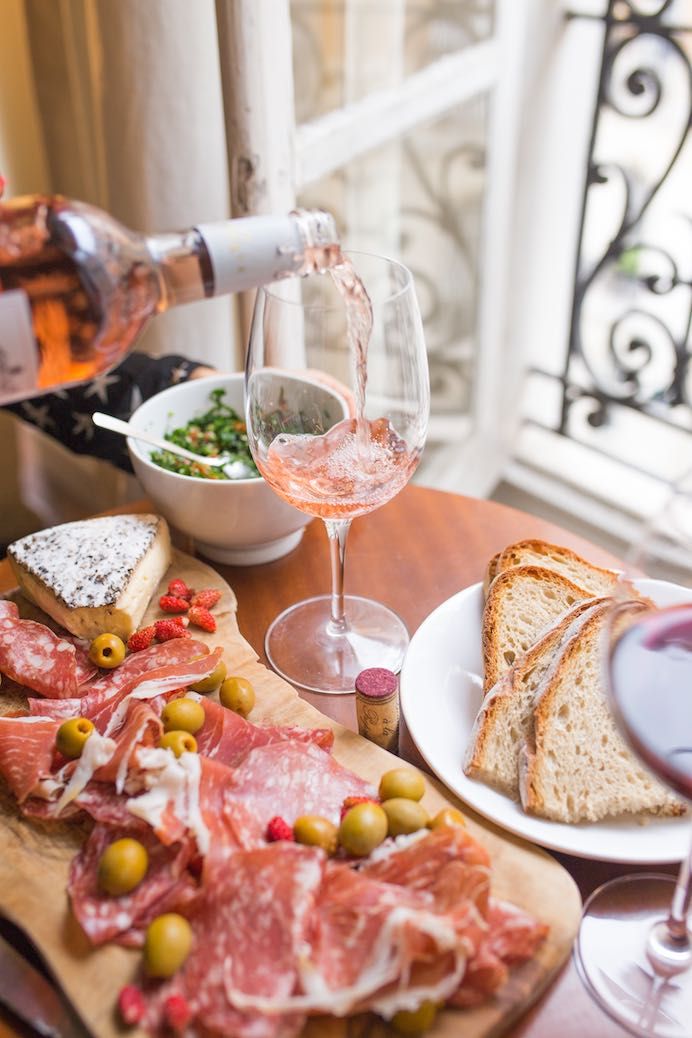 a person pouring wine into a glass on top of a table filled with meats and bread