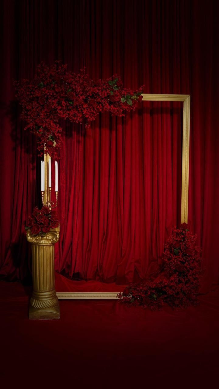 a gold vase with flowers and candles in front of a red drapeed curtain