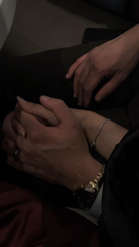 two people holding hands while sitting on an airplane seat in the dark, with their hands touching each other