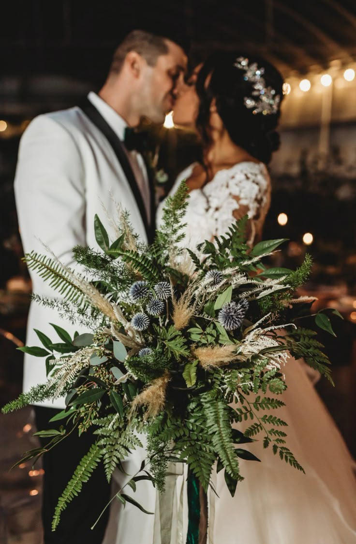 a bride and groom kissing in front of an arrangement of greenery on their wedding day