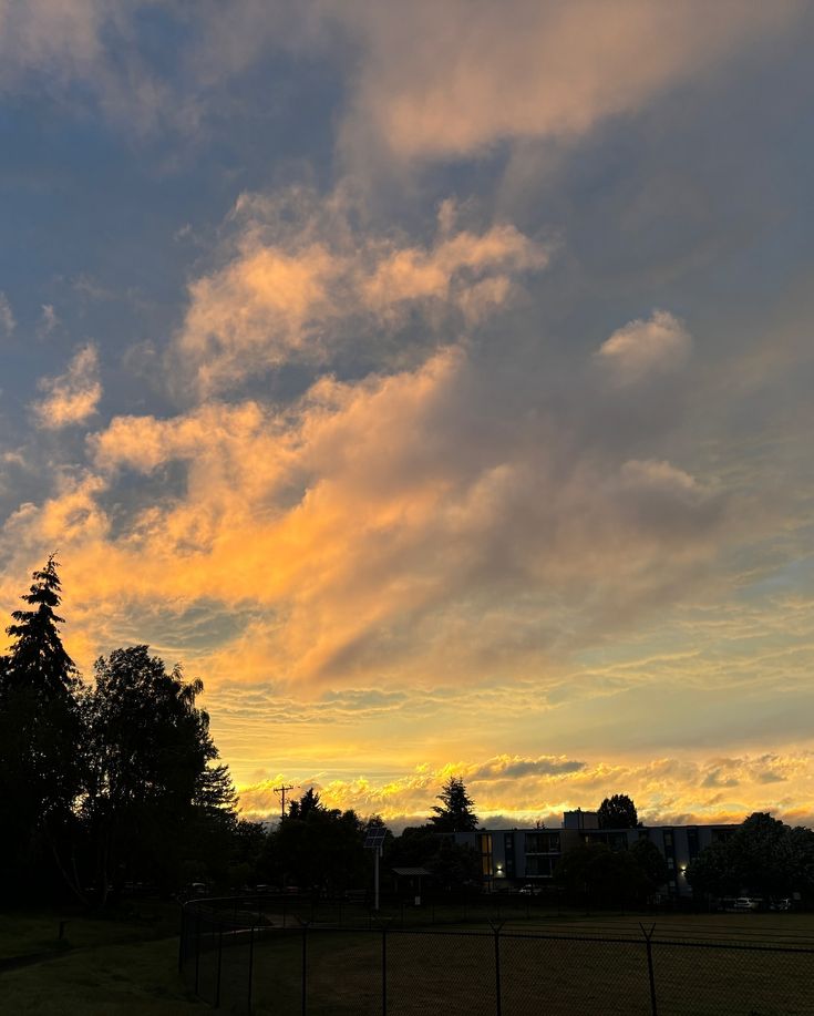 the sun is setting behind some clouds in the sky over a grassy field with trees