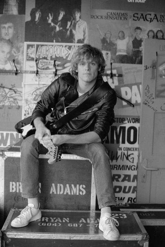 a man sitting on top of a suitcase in front of a wall covered with posters