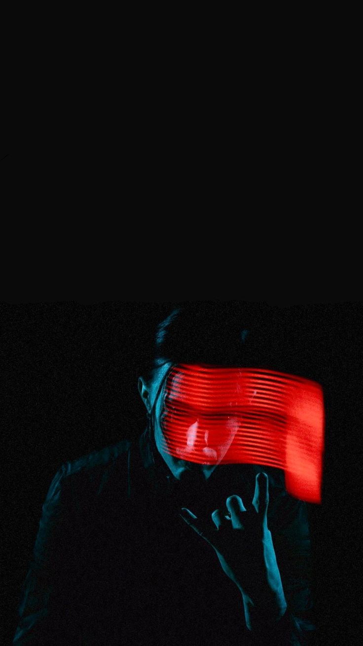 a man in the dark holding his hand up to his face with red light coming from behind him