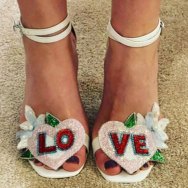 a woman's feet wearing white sandals with the word love painted on them and flowers