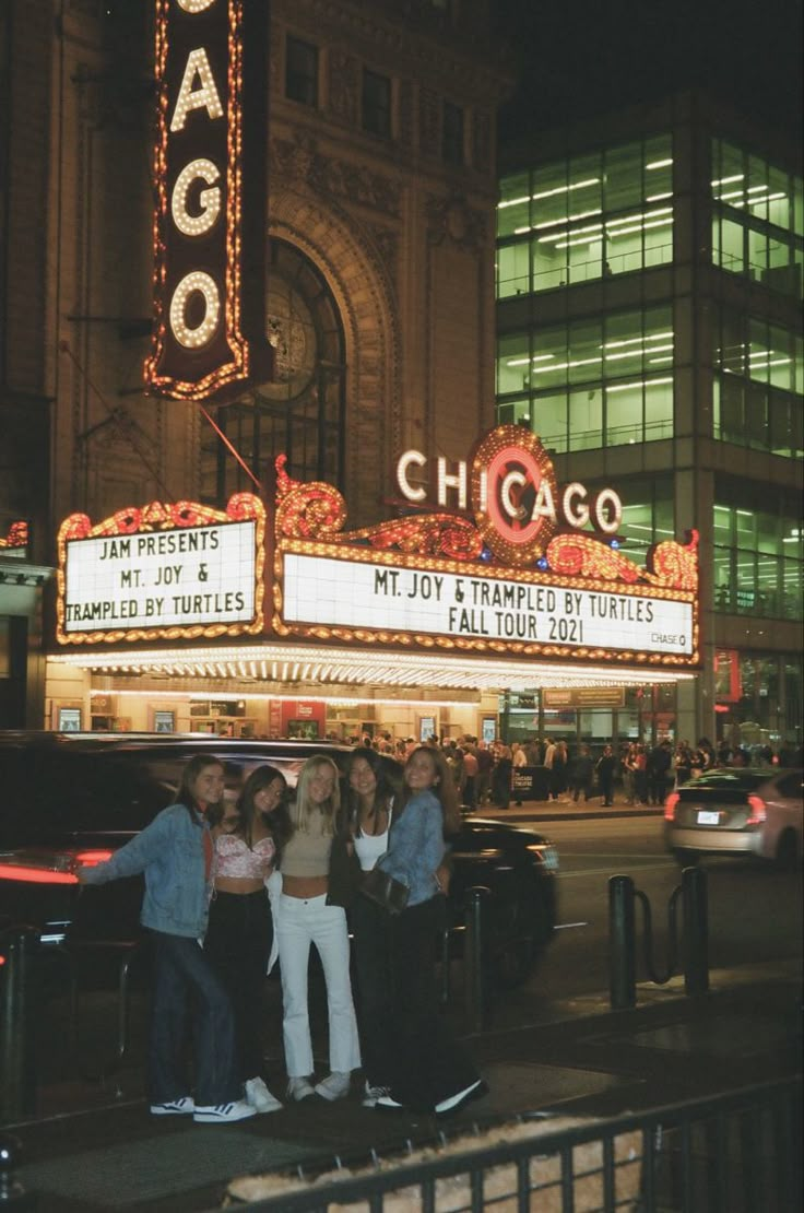 some people are standing in front of the chicago theater marquee at night time